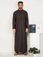  Man wearing a full-length black thobe with traditional cap, holding Hijazi branded boxes against white background