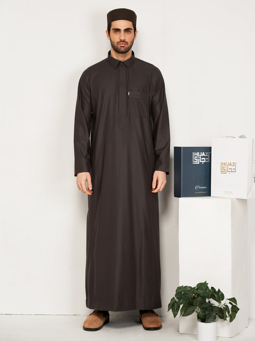  Man wearing a full-length black thobe with traditional cap, holding Hijazi branded boxes against white background