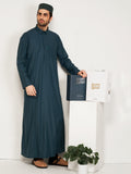 Man wearing a dark green thobe standing next to a hijazi box on a white background
