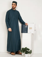 Man wearing a dark green thobe standing next to a hijazi box on a white background