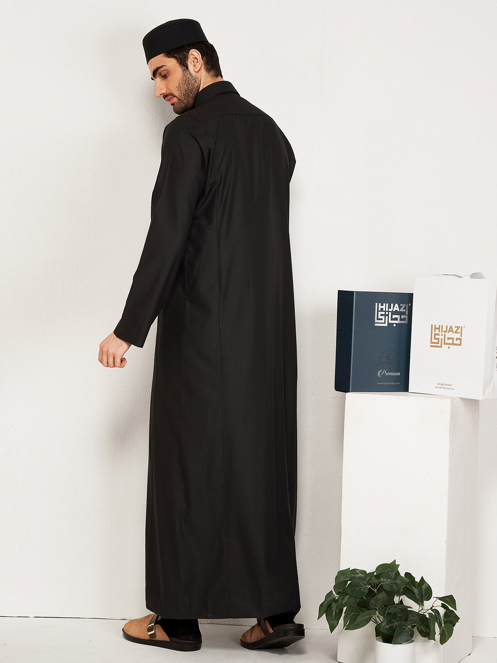 Man wearing a black abaya standing next to a white table with hijazi box on it.