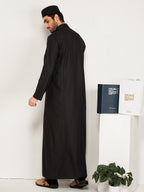 Man wearing a black abaya standing next to a white table with hijazi box on it.