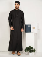 Man wearing a black traditional outfit standing next to a white stand with hijazi box on a white background