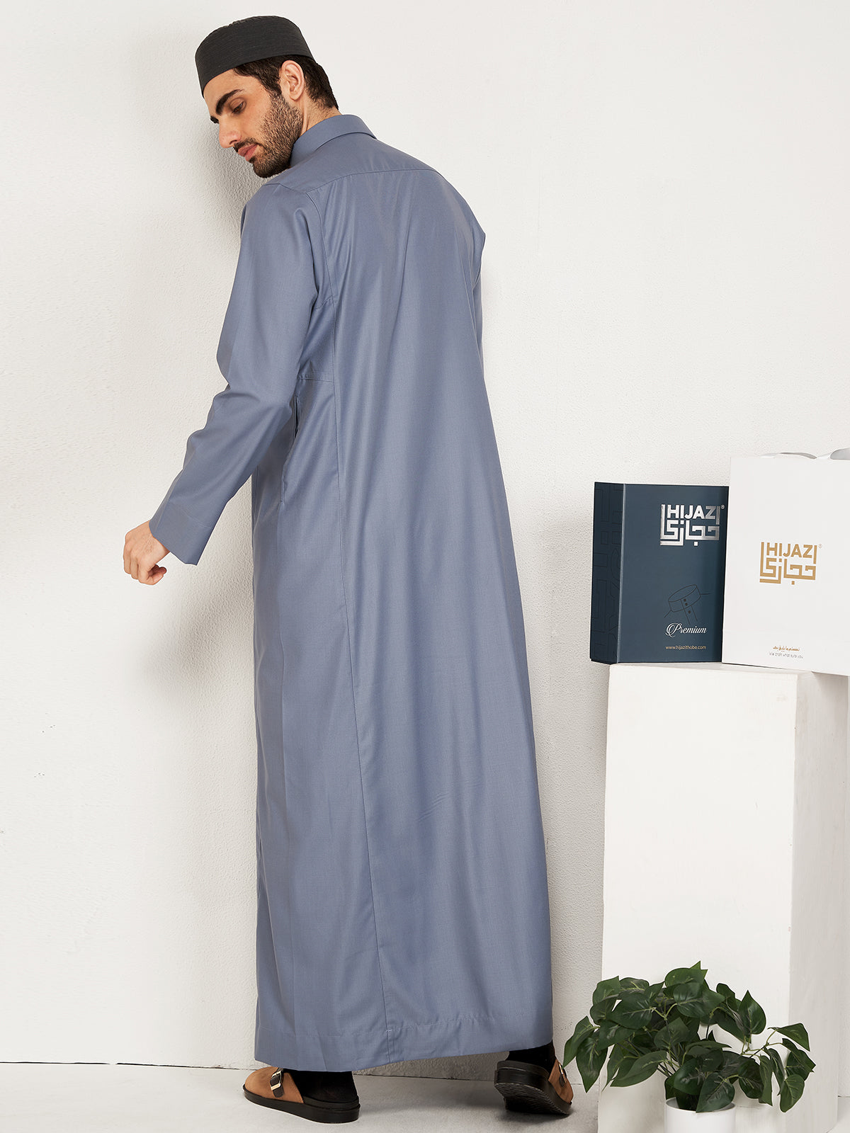 Man wearing a long greythobestanding next to a white cabinet with a Hijazi box on it.